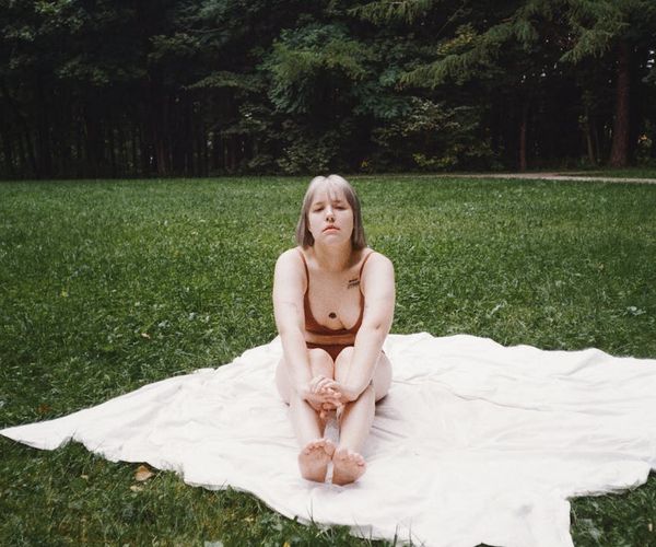 A person sitting in a calm meditative pose by a window with lush green outside.